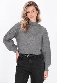 Grå ribbet striktrøje med høj krave, brede puffærmer og cropped pasform, styling med højtaljede sorte jeans og et sort bælte.