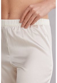 Witte broek met elastische tailleband, gemaakt van een gladde, glanzende stof. Close-up toont de textuur en pasvorm rond de taille. Minimaal detail.