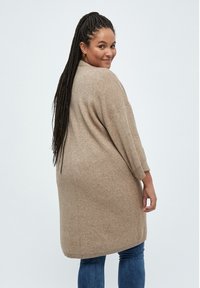 Cardigan beige oversize in maglia con maniche tre quarti, texture morbida e orlo arrotondato, abbinato a jeans blu.