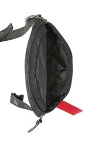 Svart tygväska med ett dragkedjeöppning, med en slät, texturerad insida och ett rött tygaccentmärke. Inkluderar justerbart remmar.