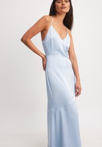 Šviesiai mėlyna satino naktiniai su V formos iškirpte, plonomis petnešomis ir prigludusia siluetu. Lygi tekstūra, grindims siekiantis ilgis su subtiliomis siūlėmis.