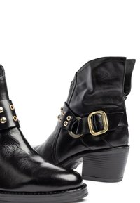 Zwarte leren enkellaarsjes met blokhakken, decoratieve gouden studs en een grote gouden gespband over de voorkant.