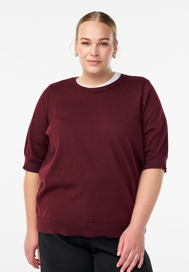 Bordeauxroter Strickpullover mit rundem Ausschnitt, kurzen Puffärmeln und geripptem Saum. Der Stoff wirkt weich und glatt mit einer strukturierten Oberfläche.