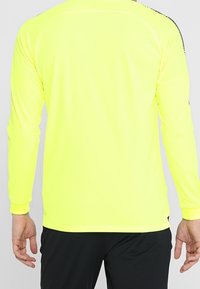 Long-sleeve athletic shirt in bright yellow, made from a smooth, lightweight fabric with black accents on the shoulders and back.