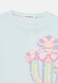 Ανοιχτό μπλε μπλουζάκι με ζωηρή στάμπα κάκτου με λουλουδένιες λεπτομέρειες, γυαλιά καρδιάς και παγιέτες. Βαμβακερό ύφασμα, κοντά μανίκια.