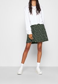 Haut blanc à manches longues et jupe verte à pois blancs. La tenue est assortie à des baskets blanches et des chaussettes montantes assorties.