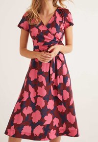 Robe portefeuille à motifs floraux avec de grandes fleurs roses et bleu marine sur un fond marron. Manches courtes et détail de taille à nouer.