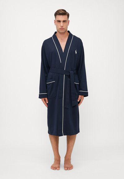 Navyblauwe badjas met witte piping, lange mouwen, zakken en een strikband. Gemaakt van zachte stof, met een klein logo op de borst.