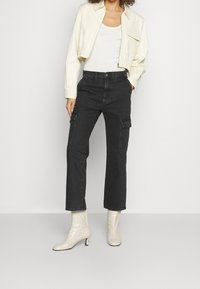 Geknipte crèmekleurige jas, aansluitend wit tanktop, zwarte cargobroek met zijzakken en glanzende beige enkellaarzen met slanke hakken.