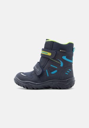 Botte d'hiver pour enfant en bleu marine avec des bandes Velcro, accents bleus et jaunes, semelle robuste et étiquette Gore-Tex pour une protection imperméable.