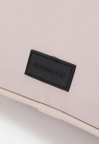 Różowa torba z tkaniny o gładkiej fakturze, z prostokątną czarną skórzaną metką wytłoczoną z nazwą marki, even&odd.