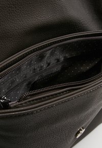 Interno di una borsa in pelle nera testurizzata con un compartimento con zip e foderato in tessuto a pois. Dettagli in hardware argentato visibili.