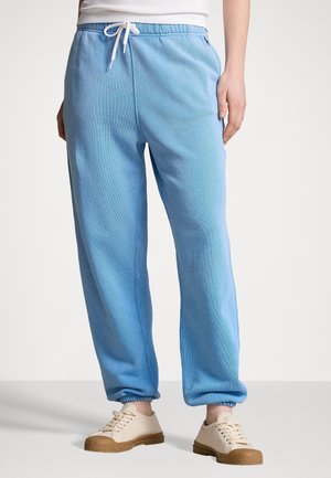 Person wearing light blue sweatpants with white drawstring and beige sneakers against a plain background.