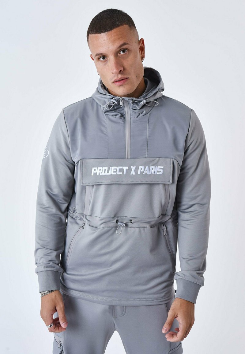 Pullover grigio chiaro con cappuccio, chiusura frontale a zip, cordino regolabile e una grande tasca sul petto. Presenta il logo "PROJECT X PARIS". Texture liscia.