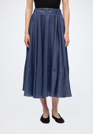 Vrouw draagt een donkerblauwe midirok met hoge taille en plooien, gecombineerd met zwarte platte schoenen en een zwart topje.
