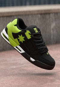 Schwarzer Skate-Schuh mit neongrünen Akzenten und einem Stern-Logo, gepolstertem Kragen, strukturierten Oberflächen und weißen Sohlen-Details.
