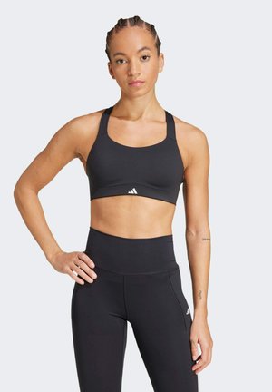 Schwarzer Sport-BH mit breiten Trägern und rundem Ausschnitt, kombiniert mit hochgeschnittenen schwarzen Leggings, die ein kleines Logo-Detail aufweisen.