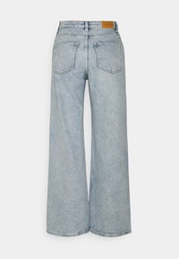 Jeans en denim bleu clair à jambes larges vus de dos, avec deux poches arrière et une étiquette de marque en cuir marron sur la ceinture.