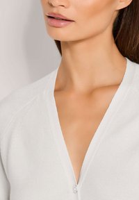 Lichtgrijze gebreide cardigan met een V-hals ontwerp, met knoopsluiting en een textiele stof, omlijst door een soepele huidskleur.