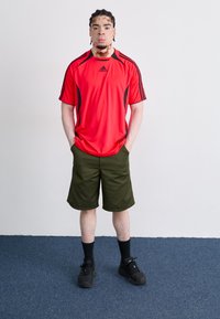 Red athletic t-shirt with black accents, paired with olive green shorts. Black sneakers and ankle socks complete the casual outfit.