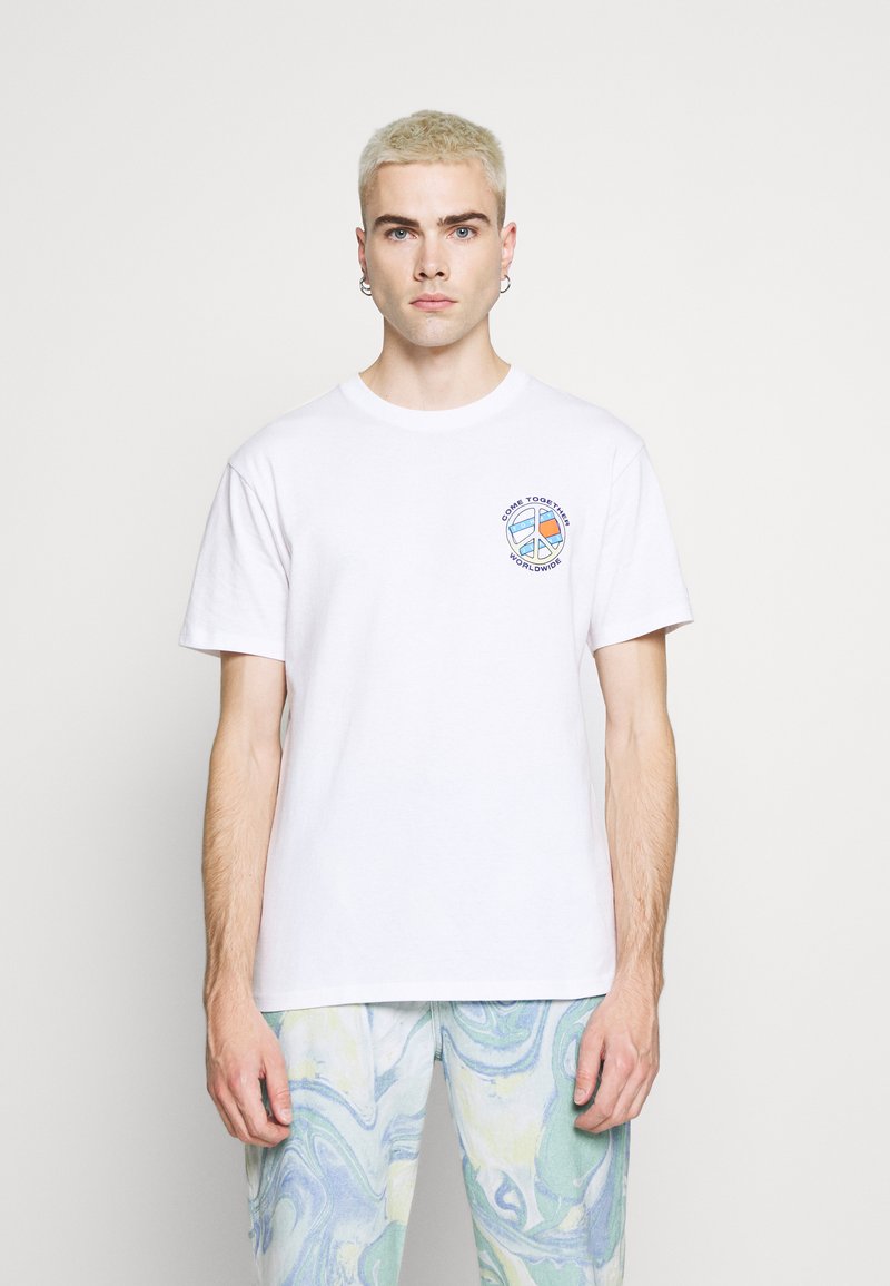 Hvid bomulds t-shirt med rund halsudskæring og korte ærmer, med et grafisk tryk i blå og sort på venstre brystområde.