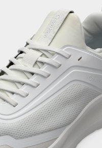 Λευκό αθλητικό παπούτσι Calvin Klein με υφασμάτινες πλέξεις στις πλευρές, παχιά σόλα και επίπεδα λευκά κορδόνια που περνούν από πλαστικά ρουχιστικά.