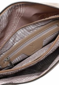 Intérieur d'un sac en tissu beige texturé avec un compartiment zippé ; doublé d'un tissu à motif marron clair avec du texte blanc et un logo.
