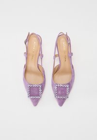 Talons slingbacks en suède violet avec des bouts pointus, ornés d'une décoration carrée avec des strass transparents. Brides de cheville réglables.