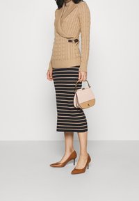 Beżowy sweter z grubym splotem, z wysokim dekoltem i boczną klamrą. Granatowa i beżowa spódnica midi w paski. Brązowe czółenka na szpic. Różowo-beżowa torebka.