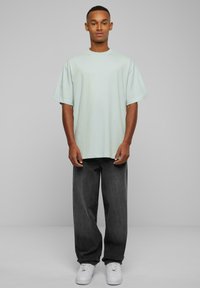 Lys myntgrønn oversized t-skjorte med korte ermer, kombinert med løse, mørkegrå jeans og hvite joggesko.