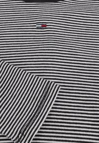 Chemise à rayures noires et blanches avec un petit logo tricolore sur la poitrine, col côtelé et tissu à texture lisse.