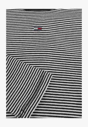 Koszulka w czarno-białe paski z małym, trójkolorowym logo na piersi, ściągaczem przy kołnierzu i gładką teksturą tkaniny.