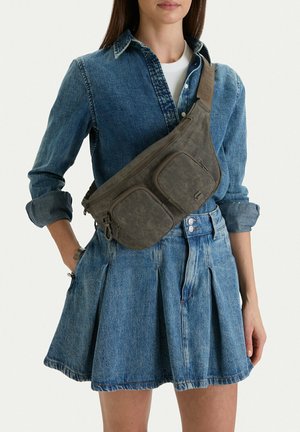Donna con una camicia di jeans blu e una gonna, con una grande borsa grigia a tracolla indossata diagonalmente sul petto.
