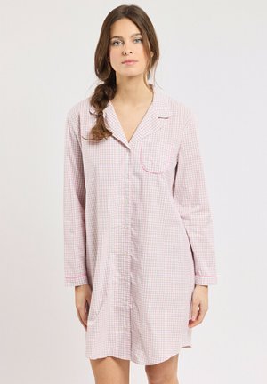 Femme aux cheveux bruns dans une tresse lâche porte une chemise de nuit à manches longues, à carreaux rose clair et blanc, boutonnée.