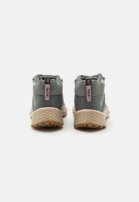 Zielone półbuty sportowe z teksturowanej powierzchni, charakteryzujące się heksagonalnym wzorem na podeszwach, różowymi akcentami oraz wzmocnionym obcasem dla większego wsparcia.