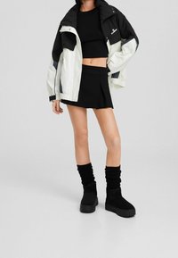 Černý crop top, bílá a černá bunda, černá plisovaná sukně, vysoké černé pletené ponožky a černé platformové boty. Neformální oblečení zaměřené na vrstvení.
