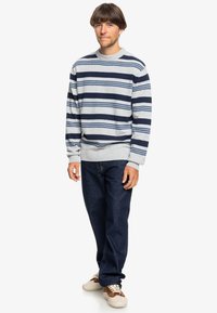 Gray sweater with dark blue and light blue stripes, knit texture, crew neck, paired with dark blue jeans and cream sneakers.
