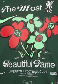 Zielona koszulka z czerwono-zielonymi wzorami kwiatowymi i motywami piłkarskimi, napisem "Najpiękniejsza Gra", logo Liverpool FC oraz brandingiem Nike.
