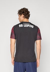T-shirt de sport noir à manches courtes avec des accents à motifs rouges. Le dos affiche "RB LEIPZIG" et la phrase "VOUS POUVEZ TOUT FAIRE."