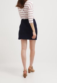 Mini-jupe brodée bleu marine avec un motif texturé, associée à un haut à rayures à manches ¾. Des sandales à talons en bois complètent l'ensemble.