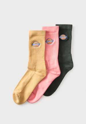 Tres calcetines de canalé en beige, rosa y negro, cada uno con un parche redondo multicolor con el logo de Dickies cerca de la parte superior.