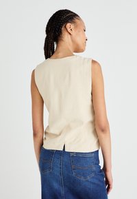 Beige ärmelloses Top mit rundem Ausschnitt, ausgestattet mit einem Schlitz in der Mitte hinten und einer glatten Textur, kombiniert mit einem blauen Jeansrock.