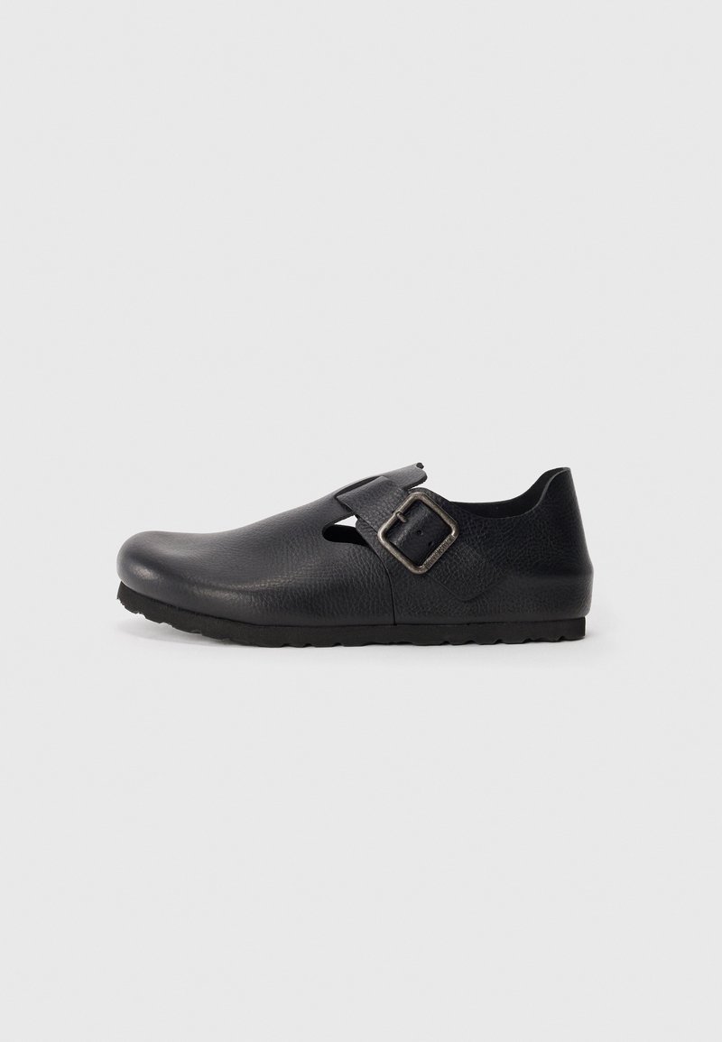 Black leather clog with an adjustable buckle strap, rounded toe, side cutout, and textured surface. Sturdy black rubber sole.