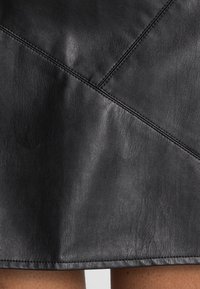 Falda de cuero negra con costuras diagonales y textura suave, con forma de A y dobladillo sin terminar. Un sutil brillo realza su apariencia.