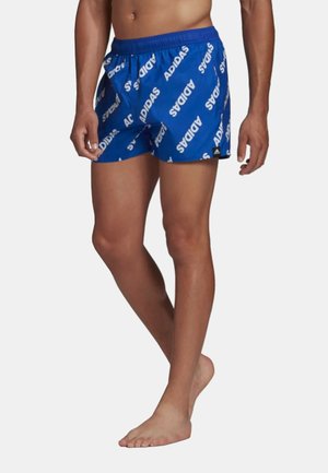 Pantaloni da bagno blu con elastico in vita, dotati di un motivo ripetuto in bianco con il logo "ADIDAS" e una piccola etichetta nera all'orlo.