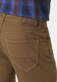 Brown cotton denim pants with a leather brand patch, visible stitching, and two back pockets featuring a pointed design.