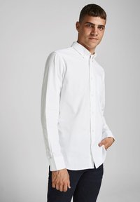 Hvit langermet skjorte med krage med knapper, enkelt brystlomme, og teksturert stoff, kombinert med mørke jeans. Rent, minimalisme design.