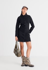 Μαύρο τζιν φόρεμα με μακριά μανίκια, κουμπιά μπροστά και γιακά. Συνδυάζεται με μεταλλικά ασημένια μποτίνια μέχρι το γόνατο και γκρι καπέλο. Τσάντα ώμου σε ελαιόχρωμο.