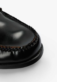 Zapato de cuero negro con punta redondeada, con un borde cosido y un acabado brillante. La suela es plana con un sutil detalle texturizado.