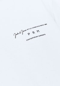 Camiseta de algodón blanca con texto negro: "Jack & Jones STYLE CONSCIOUS SINCE 1990," "PRM," y "CONTEMPORARY GARMENTS" en diferentes tipografías.